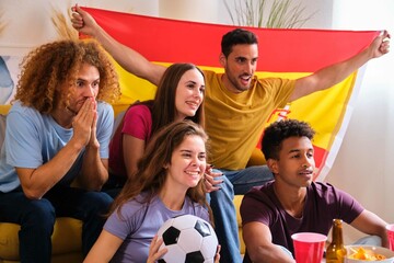 Group of friends cheering for Spain team watching the World Cup football match on TV.