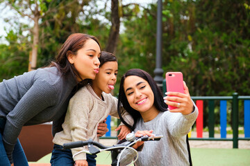 Latin lesbian couple with their son taking a funny selfie in a park. LGBT family.