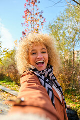 Happy young Brazilian woman smiling and taking a selfie in a park in autumn.