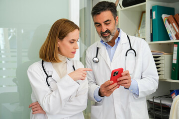 Two professional doctors talking about healthcare app and using the smartphone at office.