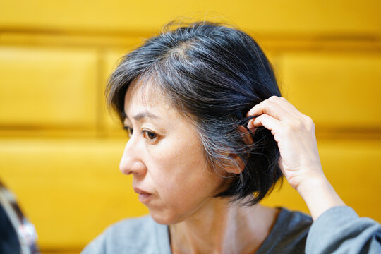 髪の毛をかき上げて生え際を見る中年女性