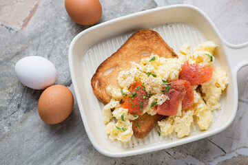Beige serving tray with scrambled eggs and smoked salmon on toast, horizontal shot on a grey granite background, high angle view