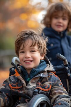 Caucasian boy with a disability sitting in a wheelchair, happy and cheerful, next to another young boy friend of his, in an outdoor park. Concept of childhood disability, companionship and friendship.