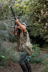 Vertical shot of a mature male in a camouflage outfit with a rifle in a forest