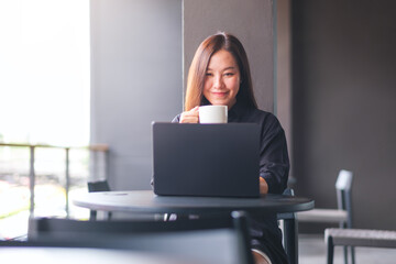 Portrait image of a young woman drinking coffee while working on laptop computer in cafe