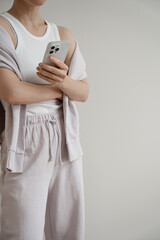 Mobile phone in female hands. Young pretty woman in neutral pastel purple sportswear over white wall. Mock up with copy space