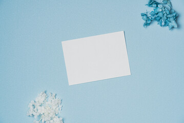 Mockup with white paper list and flowers on blue background from above. Flat lay, top view