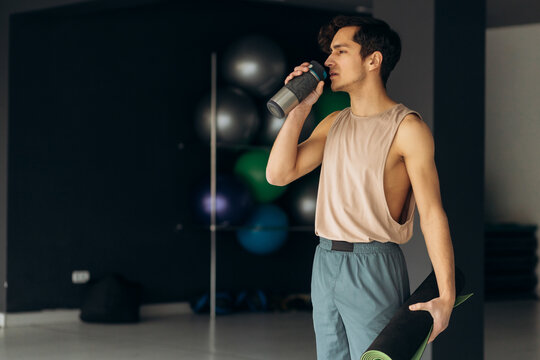 Yoga man drinks water from bottle. Handsome young man hold karimat in hand