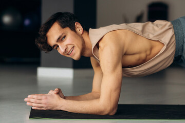 Portrait of handsome young man doing yoga plank on karemat and smile