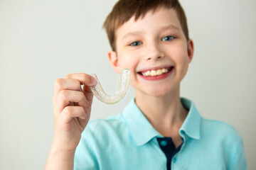 Child boy hold in hand invisible transparent aligners, invisalign bracer smile isolated on light gray background. Lifestyle concept