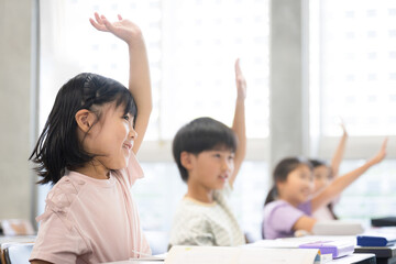 A cheerful elementary school student studying in a beautifully backlit bright classroom A Japanese child raises his hand and says, “Hi!