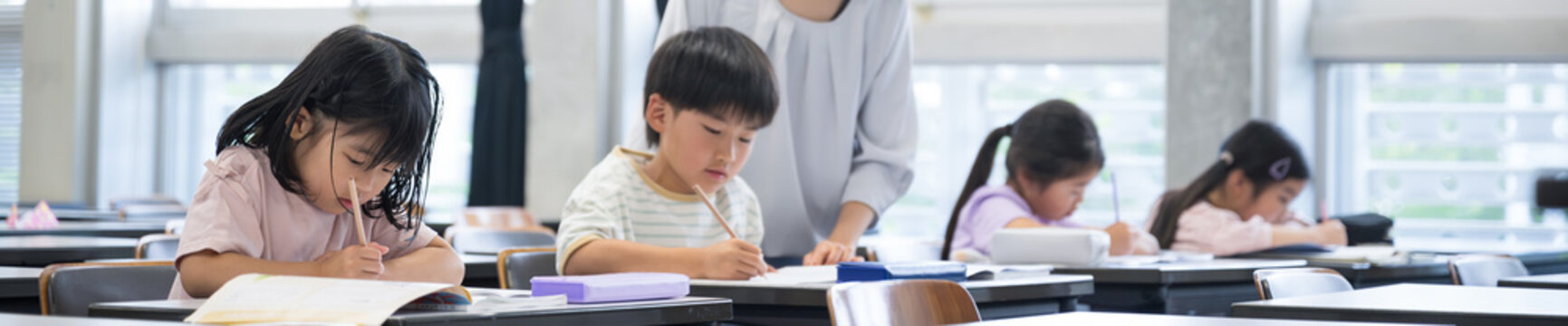 学校の教室で勉強する子供たちと指導する先生のバナー