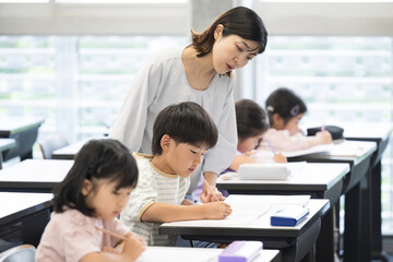学校の教室で勉強する複数(多人数)の子供たちと指導する先生