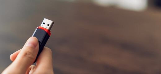 Hand holding usb flash drive with connecting to laptop at wooden table