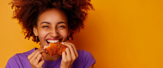 A woman is eating a piece of fried chicken and smiling. Concept of happiness. a latin woman in half about to bite a piece of fried chicken happy with a purple t shirt close-up, on a yellow background