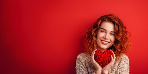 A woman with red hair is holding a red heart. The image has a warm, friendly mood. portrait of her she nice-looking attractive lovely coquettish cheerful cheery wavy-haired power girl holding in hands