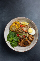 Asian cuisine. Noodles with egg and corn in a plate. On a dark background