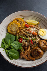 Asian cuisine. Noodles with egg and corn in a plate. On a dark background