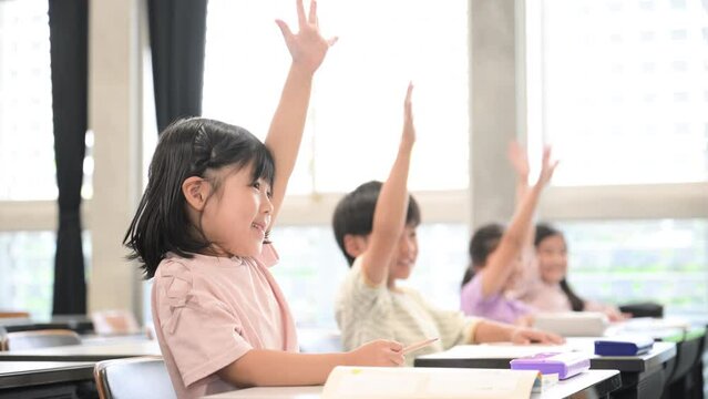 逆光の綺麗な明るい教室で授業をうけ勉強する元気な小学生 ハイと手を挙げ挙手をする