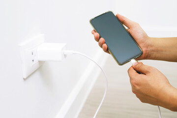 close up hand plugging adapter charge the battery with outlet socket plug and hold mobile phone on...