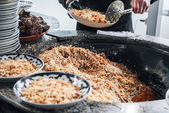 male cook cooking traditional oriental Uzbek rice pilaf in a large cauldron in the kitchen of a restaurant in Uzbekistan