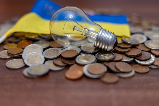 Lamp and Ukrainian flag among coins. Rising electricity prices and blackout in Ukraine due to war