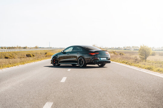 Photo of a black Mercedes-Benz AMG CLA 45 S 4MATIC+. They show details of the car from the outside. Rims, emblems, headlights, lamps in a sporty style. The model stands in the middle of highway.