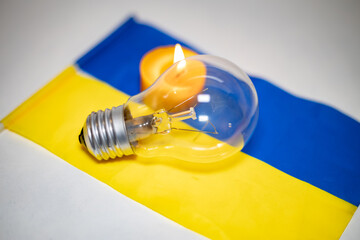 Light bulb on the background of a burning candle and the Ukrainian flag. Blackout due to the war in...