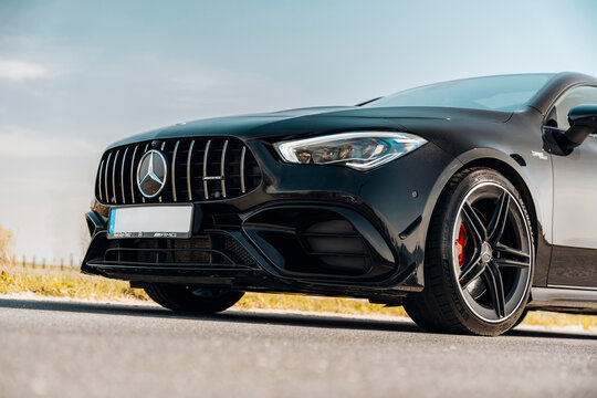 Photo of a black Mercedes-Benz AMG CLA 45 S 4MATIC+. They show details of the car from the outside. Rims, emblems, headlights, lamps in a sporty style. The model stands in the middle of highway.