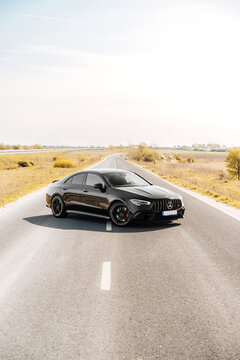 Photo of a black Mercedes-Benz AMG CLA 45 S 4MATIC+. They show details of the car from the outside. Rims, emblems, headlights, lamps in a sporty style. The model stands in the middle of highway.