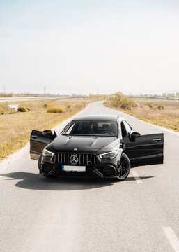 Photo of a black Mercedes-Benz AMG CLA 45 S 4MATIC+. They show details of the car from the outside. Rims, emblems, headlights, lamps in a sporty style. The model stands in the middle of highway.