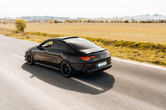 Photo of a black Mercedes-Benz AMG CLA 45 S 4MATIC+. They show details of the car from the outside. Rims, emblems, headlights, lamps in a sporty style. The model stands in the middle of highway.