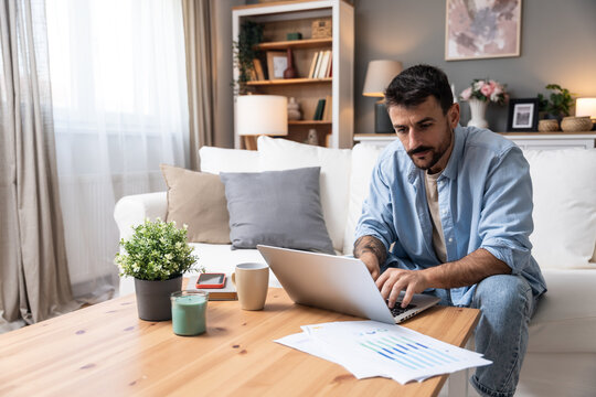 Young business man small startup company owner, working at home, checking the finances on graphs and laptop. Innovative young freelance male calculating costs and expenses of new product strategy.