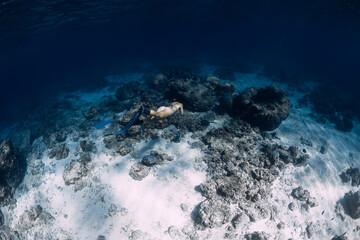 Freediver woman dives underwater to corals in blue ocean