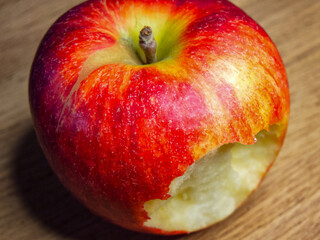 Freshly Bitten Apple. A red apple with a bite taken out, resting on a wooden surface, evoking themes of health and freshness.