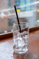 A can-shaped glass of ice with the straw on the table with bokeh background