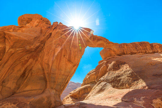 A stunning sight of the renowned Um Fruth rock bridge, featuring the natural arch and majestic sandstone formations set against a clear blue sky in Jordan's Wadi Rum desert.
