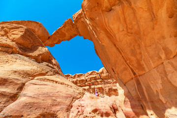 Female tourist explorer rests under the iconic Um Fruth rock arch bridge, surrounded by the...