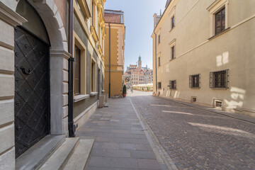 A picturesque narrow cobblestone alley leading to a historic town square, flanked by classic European buildings. The scene exudes old-world charm and architectural beauty.