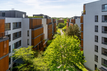 A modern apartment complex featuring sleek buildings with wooden accents, surrounded by lush...