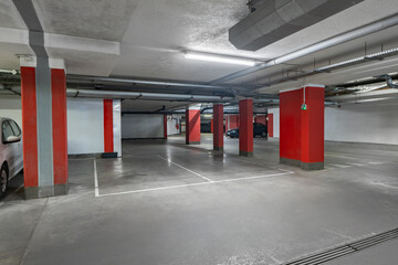 A spacious underground parking garage featuring red columns and bright lighting. The clean and...