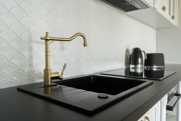 Close-up of a stylish kitchen sink featuring a gold faucet, black countertop, and elegant...