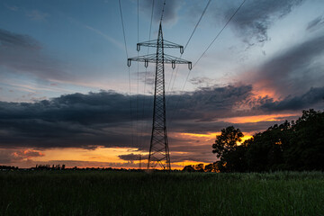 Stromtrasse ins nächste Dorf. Hochragt der Mast in den abendlichen Himmel, hinweg über Wiese und...