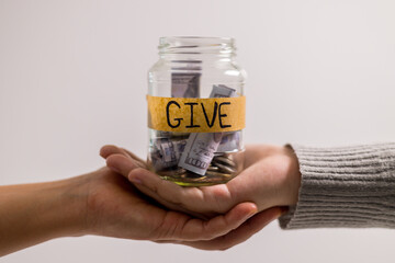 Woman holding coins and cash in jar with words Give or Donate elegantly lettered on its front, embodying spirit of giving. words, lettering, donate, jar, money, giving, woman, give, coin.