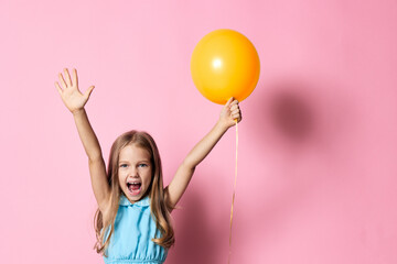 Joyful young girl holding a bright yellow balloon, smiling against a vibrant pink background
