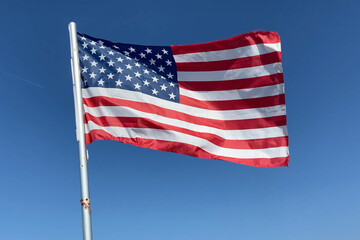 Obraz premium United State of America flag flutters in the wind on blue sky background, Travel and tourism in USA concept, election in USA 2024