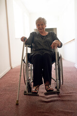 Portrait, wheelchair and senior woman in corridor with disability, retirement and smile in nursing...