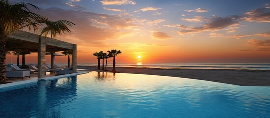 Fototapeta premium Breathtaking sunset on the beach with a pool in the foreground, ideal for a copy space image.