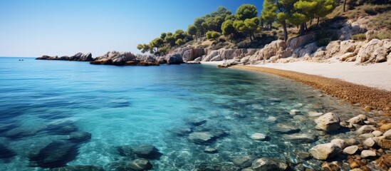 Fototapeta premium A scenic Mediterranean cove with crystal clear blue waters, surrounded by cliffs, featuring visible stones on the seabed; ideal for a copy space image.
