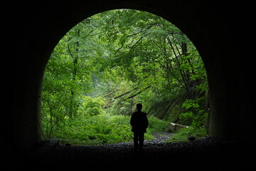 Silhouette of a man at the end of a dark tunnel. Rich green nature behind the abandoned tunnel...